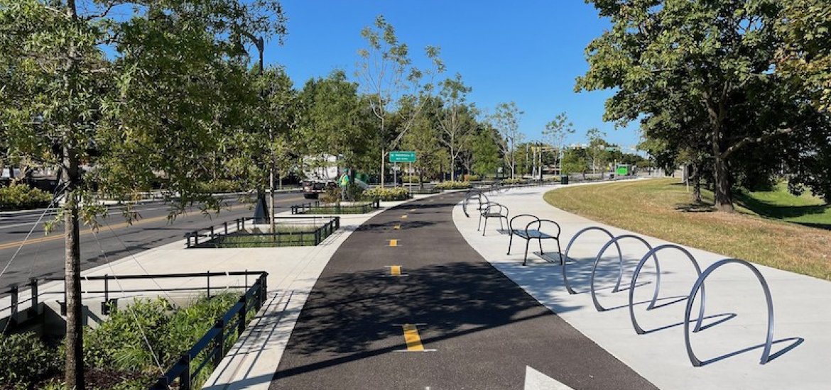 Photo of a new, asphalt-paved, 2-way bicycle lanes, with adjacent concrete sidewalks, planting areas and trees, bicycle racks, and benches. Location is the shared-use Path on Cromwell Street within the Baltimore Peninsula development.